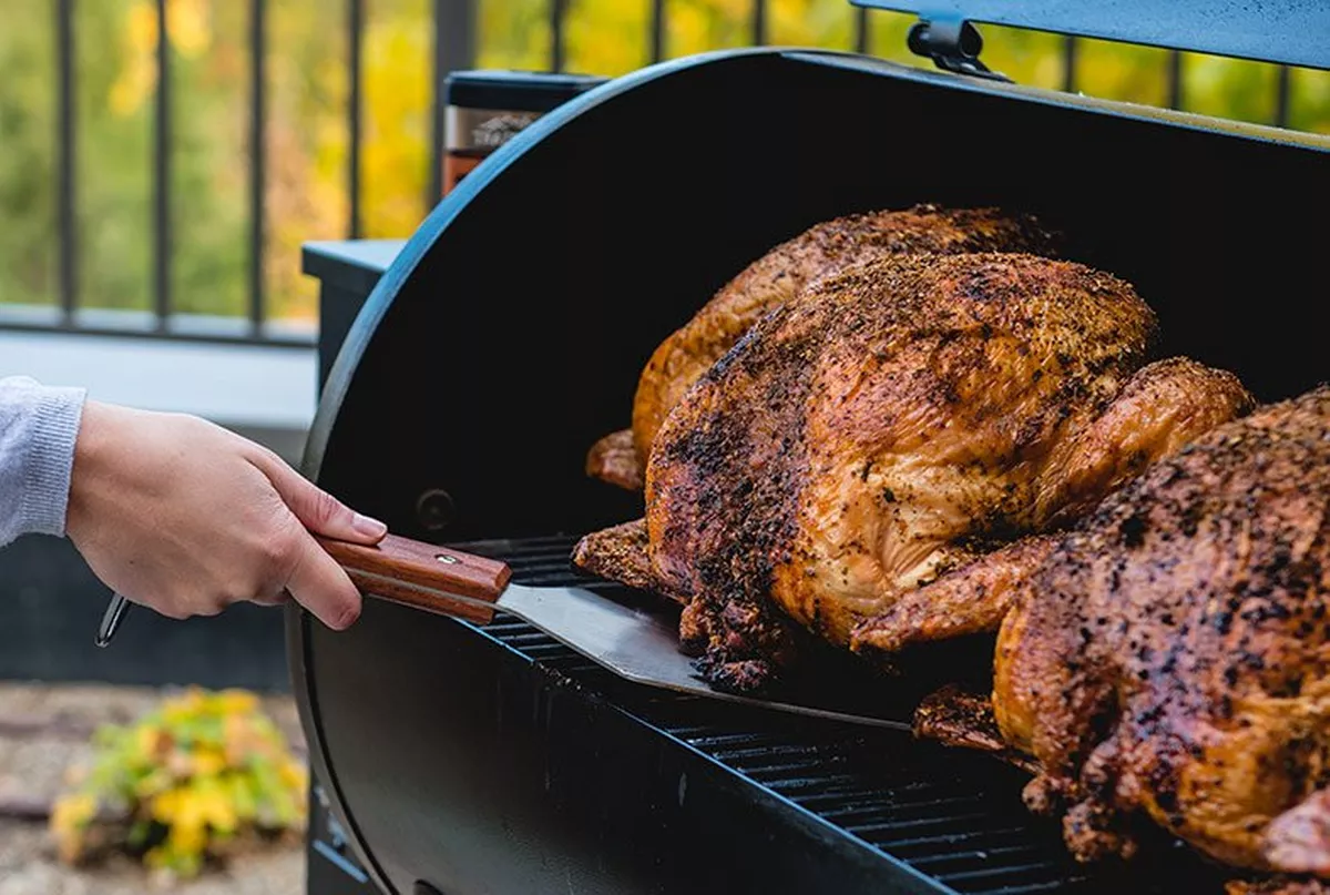 a woman picking up cooked turkey from traeger 