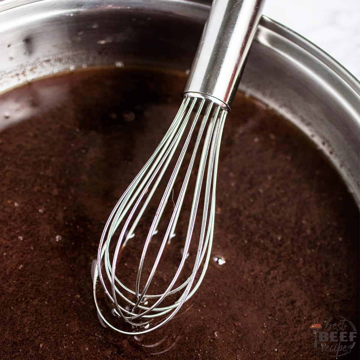whisking au jus sauce in a steel container